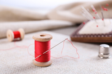 Spool of red sewing thread with needle on white fabric
