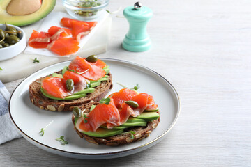 Delicious sandwiches with salmon, avocado and capers on white wooden table. Space for text