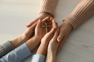 Boy and his godparents holding cross at white wooden table, closeup