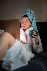 woman laying down in bed with wet head covered with towel working on laptop