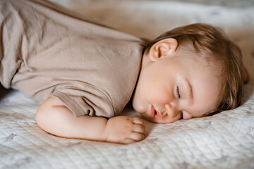 Portrait of a funny baby sleeping on his stomach on the bed at home. Close up