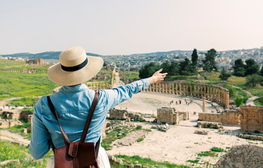 young woman tourist in color dress and hat enjoying the Oval Forum in ancient Roman city Gerasa,...