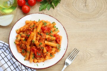 Italian Traditional Dish"Pasta al tonno e pomodorini",pasta with canned tuna in olive oil,cherry tomatoes,olive oil,onions,parsley and peppers on plate with wooden background.Top view.Copy space