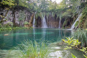 Plitvice Lakes National Park,Croatia, Europe:Waterfalls streaming into a beautiful pond with crystal clear turquoise water - surrounded by a natural finished biotope with characteristic endemic plants - obrazy, fototapety, plakaty