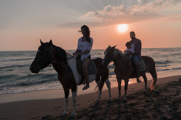 The family spends time with their children while riding horses together on a sandy beach. Selective focus 