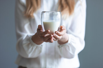 Woman hand holding glass of fresh milk on white background. Woman drinking a glass of milk in the kitchen at home. Healthy drink concept. Girl hand showing glass full of milk