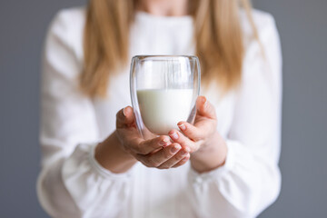 Woman drinking a glass of milk in the kitchen at home. Girl hand showing glass full of milk on gray...