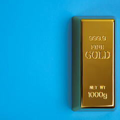 An ingot of gold metal bullion of pure brilliant diagonally located on a blue background.