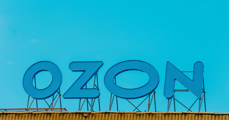 A blue Ozon sign on a building against the sky. The office of the online store in Moscow. The point...