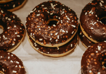 Donuts with multicolored sprinkles, isolated on a light background. Top view of donuts with chocolate glaze. Round chocolate donuts on the counter in the bakery selective focus.  Street food desserts.