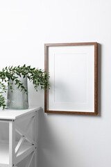 Blank portrait frame mockup for artwork or picture on white wall with eucalyptus twigs.