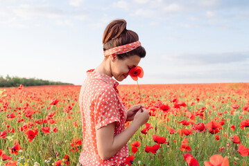 Happy smiling woman hide her smiling face in Poppy flower among red meadow.