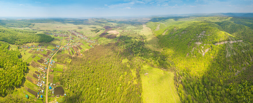 Aerial view of a remote village among dense forest and fields and mountains