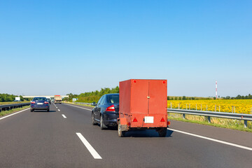 Black car with red carry-on cargo trailer on the highway.