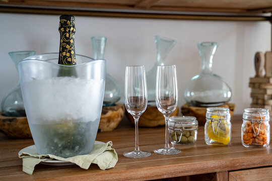 Eine eisgekühlte Flasche Champagner in einem Champagnerkühler aus Glas, daneben zwei Sektgläser sowie leckere Snacks in kleinen Einmachgläsern auf einer hölzernen luxus Bar