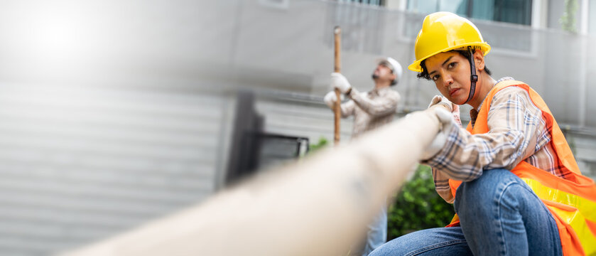 female construction worker wearing helmet and safety yellow vest checking wood On Site.Builder And Female Apprentice Carrying Wood .