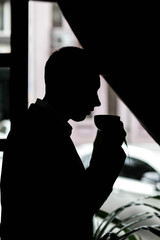 Silhouette of a man with a cup of coffee in his hands. Black and white