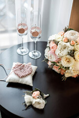 The wedding rings lie on a white pad next to the bride's bouquet. Two empty glasses. Wedding Details