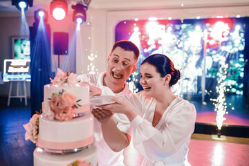 The wedding couple cuts the wedding cake with a festive vibe. The groom dares