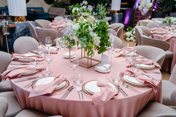 Banquet table is decorated with plates, cutlery, glasses and flower arrangements