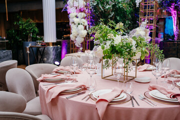 Banquet table is decorated with plates, cutlery, glasses and flower arrangements