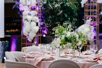 Banquet table is decorated with plates, cutlery, glasses and flower arrangements