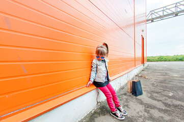 Little stylish girl in sunglasses with craft bags on a shopping trip on an orange background.