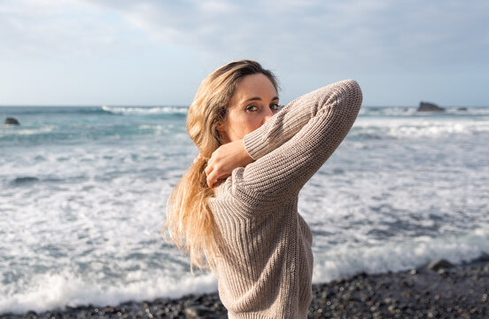 Portrait of a beautiful blonde-haired young woman on the beach with a beige sweater