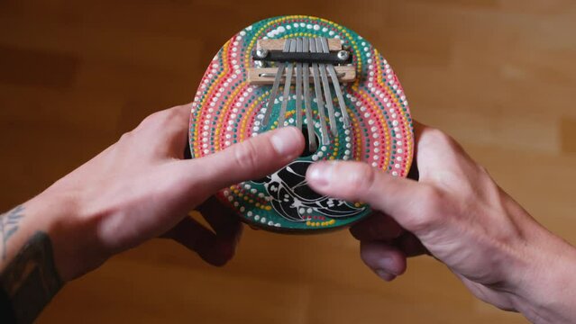 Close-up of male fingers playing the kalimba musical instrument. Authentic thumb piano being played by musician. Colorful traditional wooden african mbira instrument used by caucasian artist
