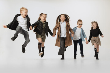 Happy school and preschool age children, girls and boys running, jumping isolated on grey studio background. Beauty, kids fashion, education, happy childhood concept.