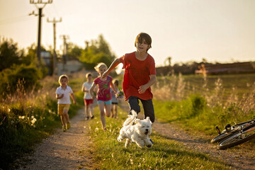 Happy group of children and pet dog, maltese breed, running in the park on sunset, carefree...