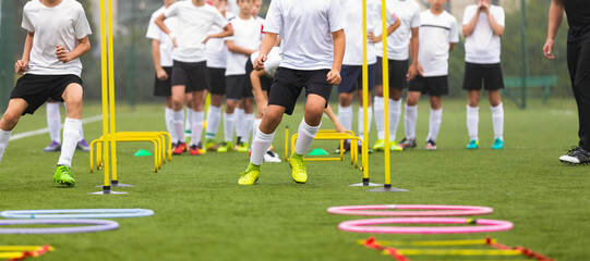 Young Boys Running Slalom Track Between Training Poles and Jumping Over Ladders. Teenage Football Players Running in Two Rows on Training Camp. Soccer Training Equipment