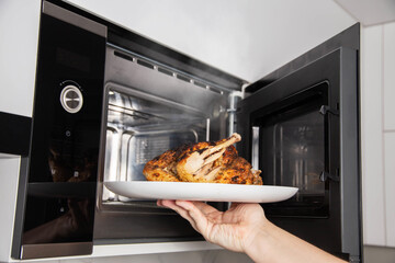 A man takes a plate of grilled chicken out of the microwave. The concept of using modern microwave ovens with grill and convection, close-up