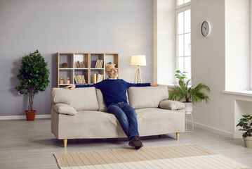 Senior man sitting on comfortable couch at home. Happy mature man relaxing on comfy grey sofa in...
