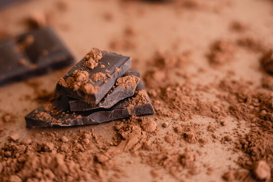 Close up view of natural cocoa powder and chocolate on blurred brown background.