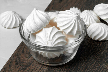 The dessert of French meringue lies in a glass vase on a dark wooden board on a gray background. there are whole and broken meringues lying around. close-up.