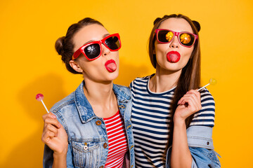 Portrait of two careless crazy people hold lollipop show tongue out isolated on yellow color...