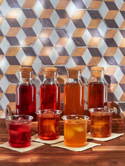 Four bottles and four glasses of cold brew fruit tea, rooibos, green and black, in a wooden tray on a wooden table