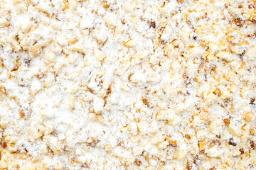 Part of sweet cake with white powder, cream and broken nuts, top view as texture, background and space for text