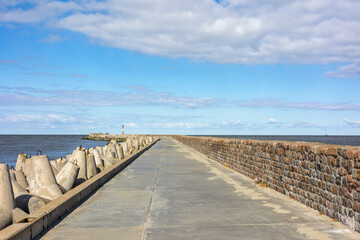 A concrete pier with a brick fence goes into the sea. A clear sunny day and a blue sky with clouds in Baltiysk, Kalinigrad region, Russia, near the Baltic sea.