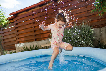 A happy little girl jumps into the pool and splashes, splashes of water splatter in different...