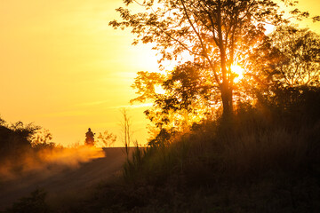 Man riding a motorcycle on a dirt road during the sunset .