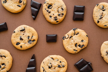 Top view of chocolate pieces near cookies on brown background.