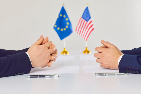 Relationship between European Union and America. US and EU diplomats sit opposite each other in meeting on contracting and business regulation. Close up of hands of representatives on table.