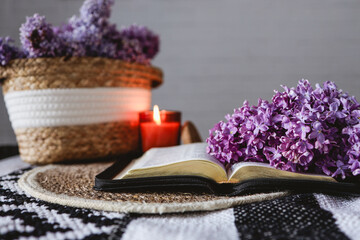 An open Bible with a lilac branch, a wicker basket and a candle on the table. Beautiful aesthetic good morning picture