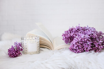Obraz na płótnie Canvas An open book with a lilac branch and a candle on a white fluffy plaid. Beautiful card. Good morning concept