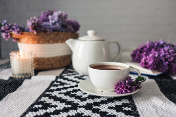 Obraz na płótnie Canvas A cup of tea with a teapot on a table with a lilac wicker basket, atmospheric tea party photo