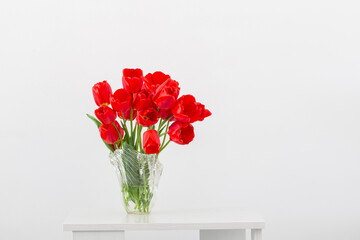 red tulips in glass vase on background white  wall