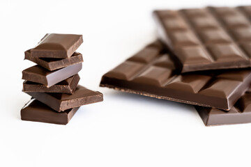 Close up view of pieces of dark chocolate near blurred bars on white background.