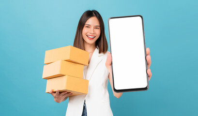 Smiling beautiful Asian woman holding cardboard boxes and hands show smartphone mockup of blank...